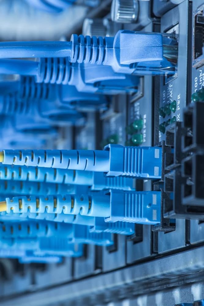 Cabos de rede azuis conectados a um switch, representando infraestrutura de cabeamento estruturado para casas inteligentes.
