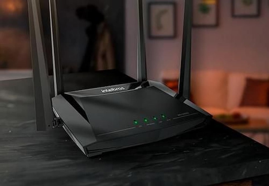 Roteador Intelbras preto com antenas em ambiente residencial iluminado.

