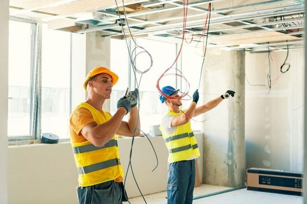 Dois profissionais passando cabos no teto durante obra em fase de infraestrutura, com foco em automação residencial.